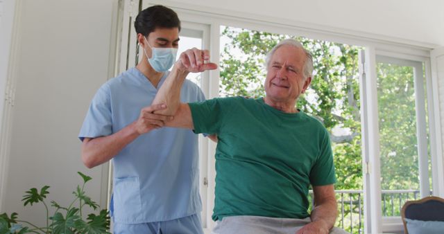 Senior man wearing green t-shirt receiving assistance for physical therapy exercises from healthcare professional in home setting. Keywords emphasize elderly care, physical rehabilitation, and patient treatment at home. Useful for articles or promotional materials on home healthcare, elderly wellness, or physical therapy services.