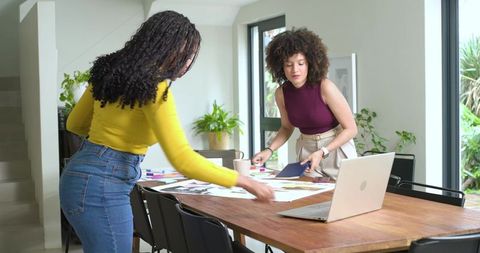 Diverse female teammates collaborating on design mockups in bright home workspace