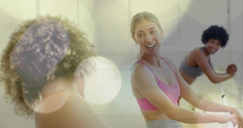 Smiling woman in pink sportswear doing barre with group at bright fitness studio