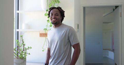 Smiling african american man standing near window in bright modern apartment with plants