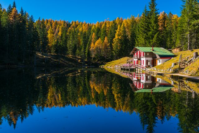 Idyllic scene featuring a cozy cabin by a calm lake reflecting vibrant autumn colors. Perfect for use in travel ads, relaxation retreats, and nature-themed designs highlighting tranquil outdoor escapes.