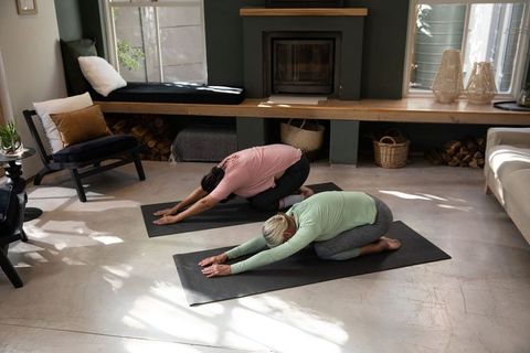 Mature women practicing restorative yoga on mats in cozy sunlit living room with fireplace