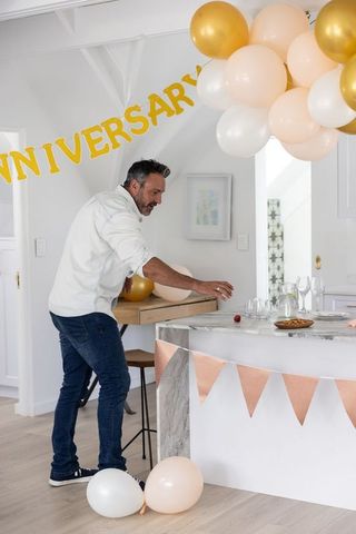 Man arranging anniversary decorations in kitchen with gold balloons and marble island
