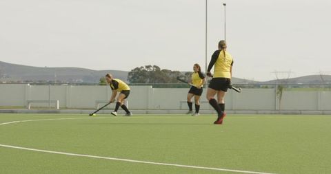 Female athletes playing field hockey outdoors, teamwork focus
