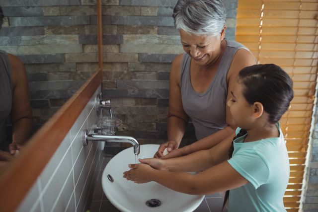 Grandmother and granddaughter washing hands in bathroom sink at home