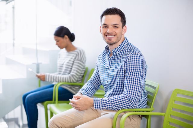 Portrait of smiling man sitting on chair in hospital corridor