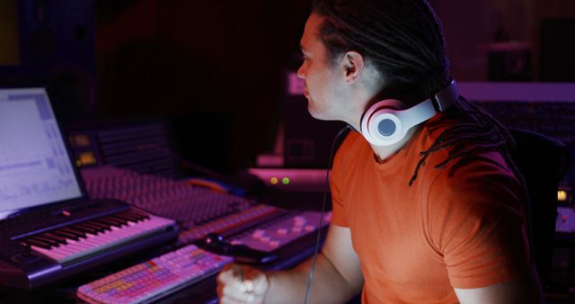 Music producer using computer and equipment to mix audio in recording studio at night. Ideal for content related to music production, sound engineering, professional audio work, and creative studio environments.