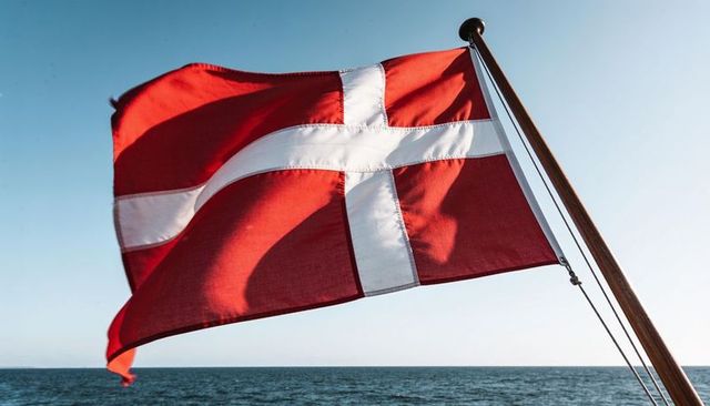 Danish flag waving on wooden mast at sea, red ensign with white nordic cross billowing