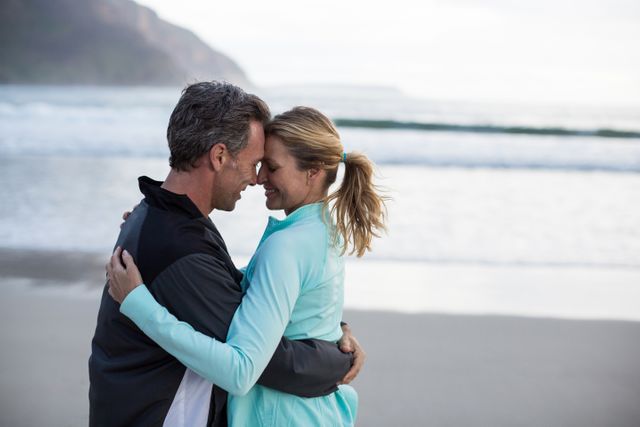 This warm and heartfelt image shows a mature couple embracing on a beach at sunset. It is perfect for use in advertisements, travel brochures, romantic getaway promotions, or articles on relationships and love. The affectionate pose and beautiful scenery make it ideal for themes related to romance, connection, and seaside vacations.