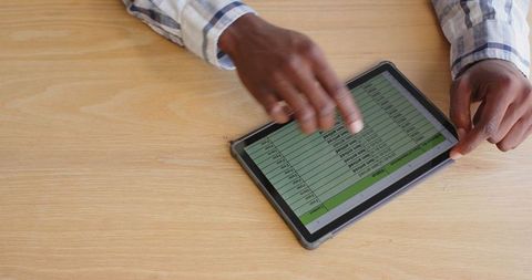Hands analyzing spreadsheet data on tablet at office desk