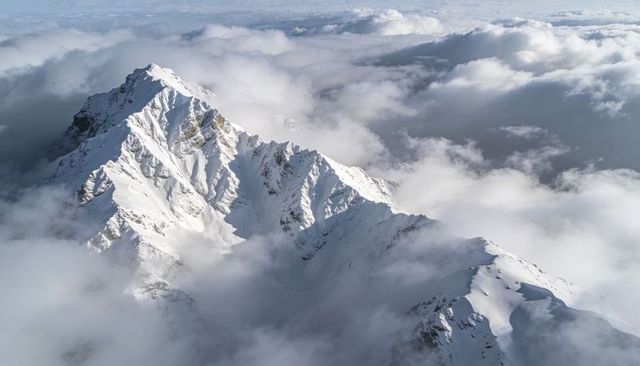 Sunlit Snow Ridge Rising Above Clouds Aerial Alpine Panorama with Jagged Peaks and Cornices