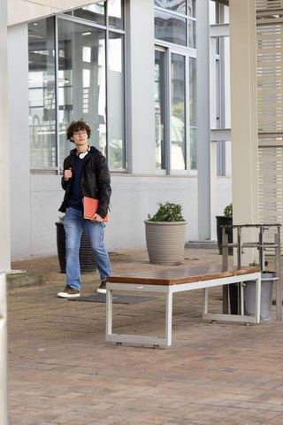 Teenage student walking on modern campus walkway carrying red folder and headphones