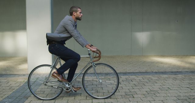 Business man cycling in city wearing suit jacket and jeans, epitomizing eco-friendly transportation in an urban setting. Ideal for topics on sustainable commuting, urban lifestyles, combining professionalism with healthy living, and promoting bicycle use for daily travel.