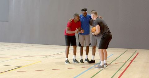 Huddling basketball teammates planning offensive play on indoor gym court, teamwork focus