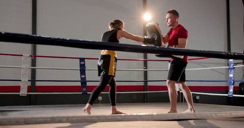 Male coach training female boxer delivering focused punches on mitts inside boxing ring