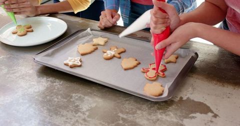 Diverse friends decorating festive gingerbread cookies in kitchen