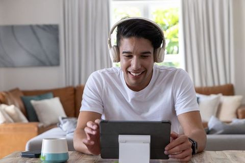 Smiling african american man using tablet with headphones at bright home workspace