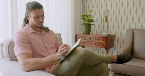 Man in pink shirt writing in notebook on sofa