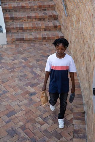 Urban teen walking through brick courtyard holding brown paper bag