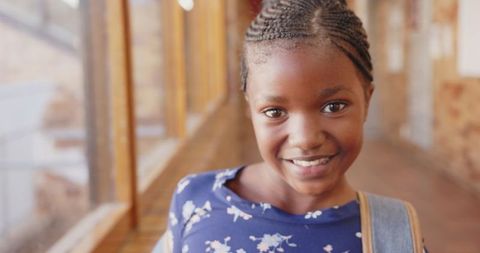Smiling African American Girl in School Corridor Holding Backpack Strap