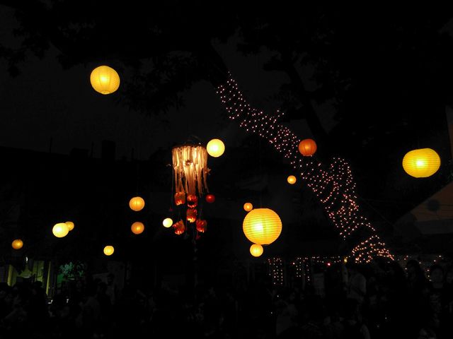 This image captures the ambiance of an outdoor night festival, showcasing hanging lanterns and string lights glowing in the dark. Suitable for content related to festivals, celebrations, parties, and illuminating decorations. Useful for blog posts, background images, event promotions, and web content portraying lively nighttime events.