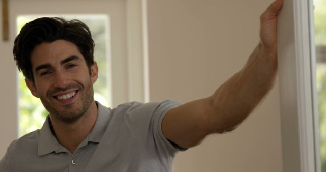 A young Caucasian man is smiling and waving in a welcoming gesture, with copy space. His friendly demeanor suggests he might be greeting someone or inviting them into his home.