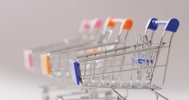 Mini shopping carts with colorful handles lined up sequentially. Perfect for illustrating concepts related to retail, consumerism, or marketing. Ideal for use in blog posts, e-commerce, presentations, or advertisements focused on shopping and retail industry.