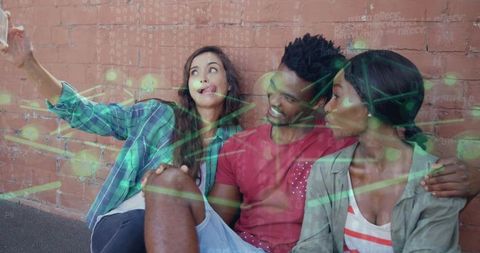 Friends taking selfie on red brick wall with green network overlay, casual trio on pavement