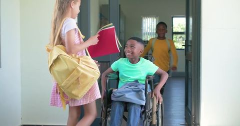Schoolchildren chatting at doorway with smiling boy in wheelchair and girl holding red folder