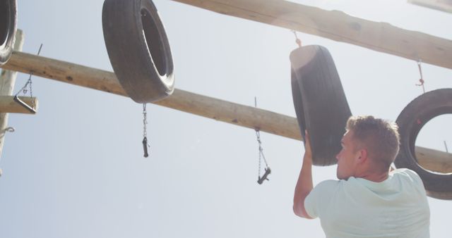 Young man participating in an outdoor obstacle course, engaging with a tire challenge. Perfect for depicting themes of fitness, outdoor activities, competition, and physical endurance. Useful for fitness promotions, training programs, sports equipment advertisements, and motivational content.