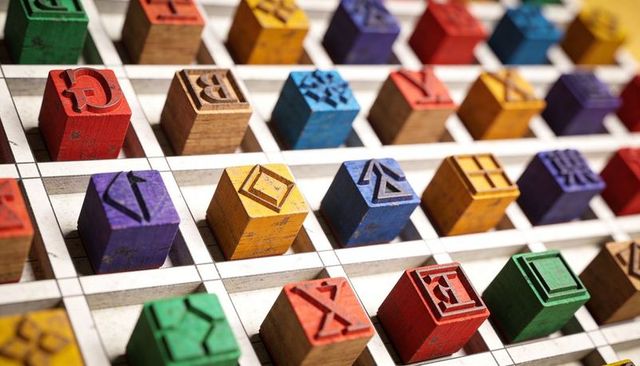 Displaying colorful carved wooden letter and symbol cubes in white grid close-up