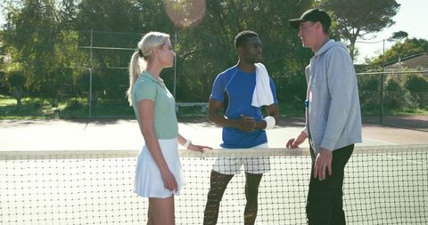 Tennis coach mentoring two players at net discussing strategy on sunny outdoor court
