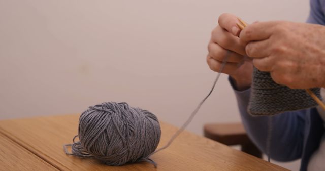 Senior hands knitting grey wool with wooden needles at wooden table - Download Free Stock Images Pikwizard.com