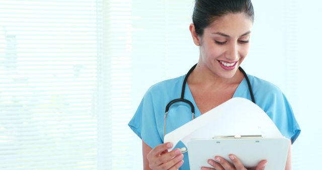 A young Asian female nurse reviews a patient's medical records, with copy space. Her professional demeanor and smile suggest a positive interaction in a healthcare setting.