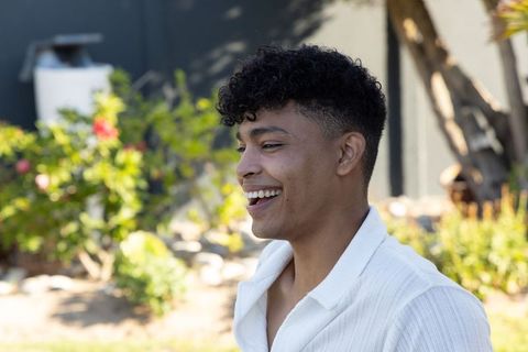 African american man smiling in sunlit backyard wearing white shirt, candid summer portrait