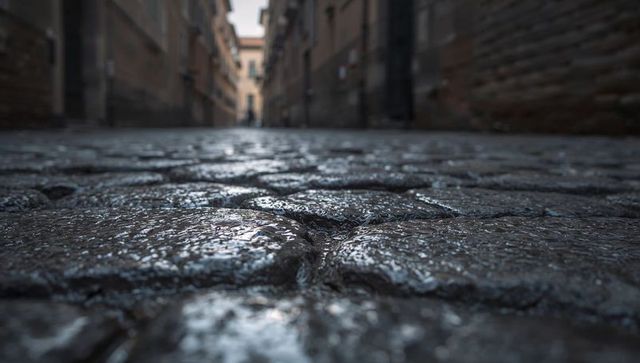 Glistening wet cobblestone alley reflecting light on damp narrow urban stone street