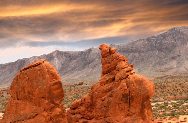 Spectacular view of desert rock formations against a dramatic sunset sky with mountains in the background. Ideal for use in travel brochures, nature photography collections, geology studies, and outdoor adventure advertisements. Perfect for conveying the beauty and ruggedness of desert landscapes.