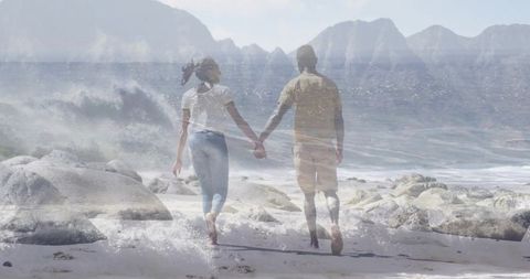 Couple Holding Hands Walking Along Rocky Beach Toward Waves
