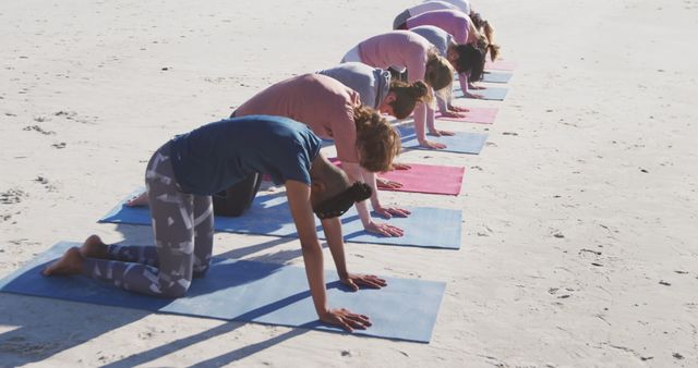 Group of individuals stretching on yoga mats on a sandy beach. Participants enjoying outdoor group yoga class with a focus on health and wellness. Ideal for use in content about fitness routines, beach activities, yoga classes, and outdoor exercise programs.