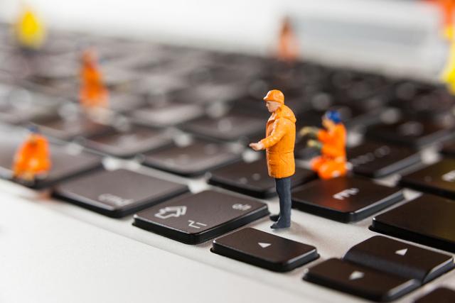Miniature workmen are seen repairing a laptop keyboard, symbolizing the concept of technology maintenance and repair. This image can be used in articles or advertisements related to tech support, computer repair services, or technology maintenance. It is also suitable for illustrating concepts of teamwork, precision, and attention to detail in a business or office environment.