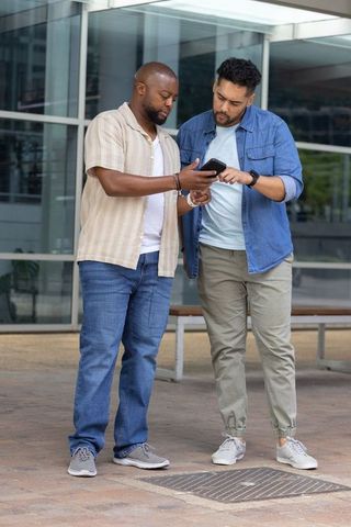 African american men collaborating over smartphone outside modern office building