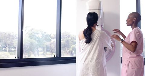 Woman Undergoing Mammogram While Radiology Technician Guiding Positioning in Bright Clinic