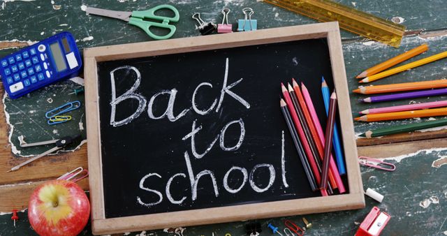 A chalkboard with the words Back to School is surrounded by school supplies like pencils, scissors, and an apple, with copy space. It symbolizes the start of a new academic year and the preparation involved.