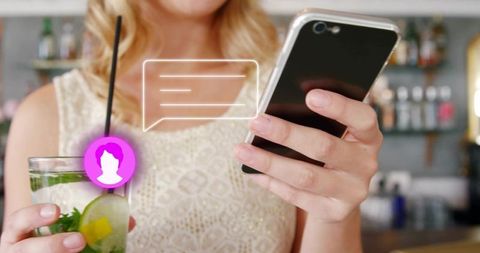 Woman checking phone holding mint lime cocktail at bar with chat notification