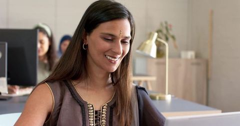 Indian woman in embroidered kurta working on laptop and smiling in open-plan office