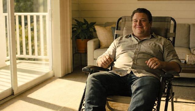 Sunlit man relaxing in reclining chair by sliding glass door at home, casual denim comfort