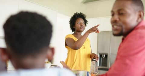 African american family cooking in bright kitchen, mother pointing while grating carrot
