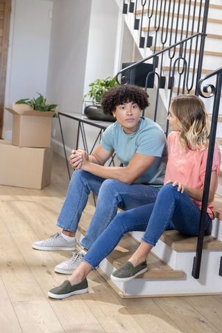 Young diverse couple sitting on stairs talking while moving into modern home