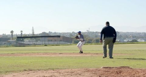 Baseball pitcher preparing to throw with umpire on mound in sunny suburban ballpark action