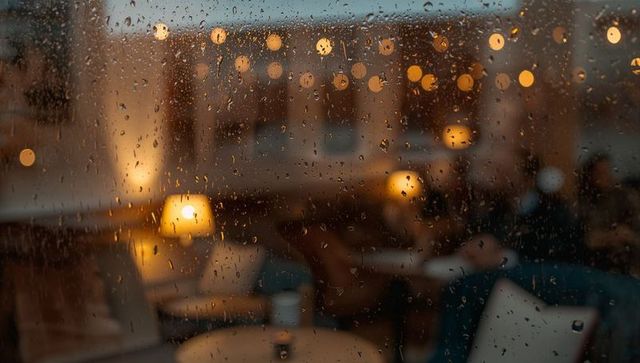 Raindrops clinging to window filtering warm cafe lights and cozy bokeh lounge glow evening ambience